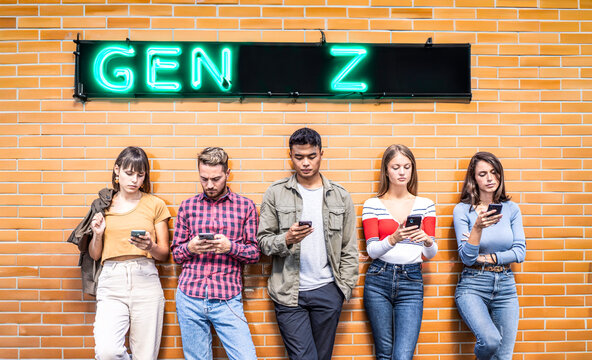 Group of gen z young adults using smartphones under neon sign in urban setting. Modern youth culture showing digital lifestyle, social media use and mobile communication.