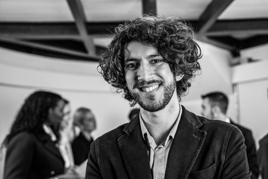 Smiling young businessman working inside modern office with the multiethnic team behind him - Concept of leadership and achieving goals - Focus on eyes - Black and white editing