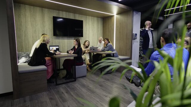 Business professionals engage in collaborative work and discussion within a modern office setting. The team analyzes data and brainstorms ideas in a corporate meeting space.