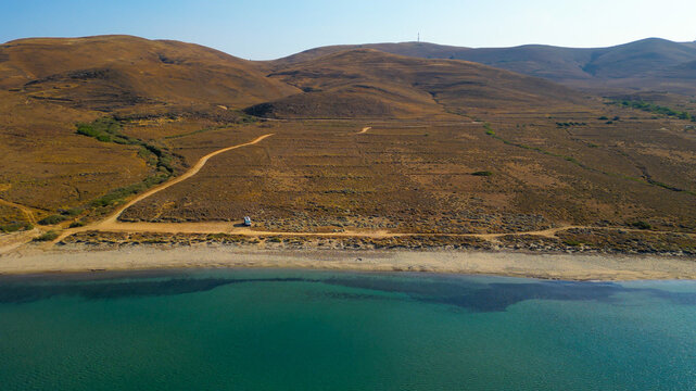 Aerial drone view of a parked campervan at beach Parthenomitos on Limnos Island, Greece. Remote Mediterranean coastal landscape with turquoise sea, rocky shoreline, and peaceful free camping