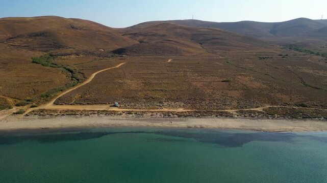 Aerial drone view of a parked campervan at beach Parthenomitos on Limnos Island, Greece. Remote Mediterranean coastal landscape with turquoise sea, rocky shoreline, and peaceful free camping