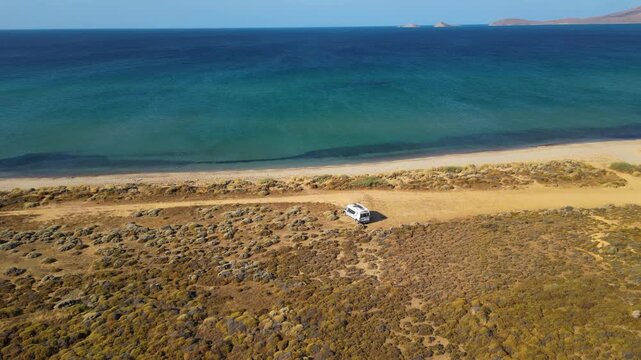 Aerial drone view of a parked campervan at beach Parthenomitos on Limnos Island, Greece. Remote Mediterranean coastal landscape with turquoise sea, rocky shoreline, and peaceful free camping