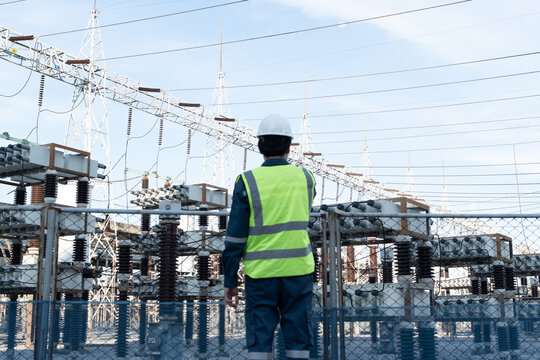 Engineer stands in a high voltage substation for grid monitoring, supporting power system inspection, asset reliability, operational safety, and utility infrastructure oversight.