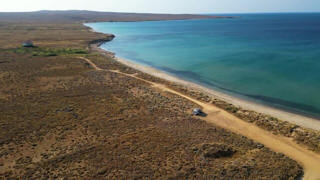 Aerial drone view of a parked campervan at beach Parthenomitos on Limnos Island, Greece. Remote Mediterranean coastal landscape with turquoise sea, rocky shoreline, and peaceful free camping