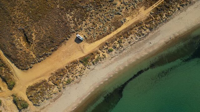 Aerial drone view of a parked campervan at beach Parthenomitos on Limnos Island, Greece. Remote Mediterranean coastal landscape with turquoise sea, rocky shoreline, and peaceful free camping