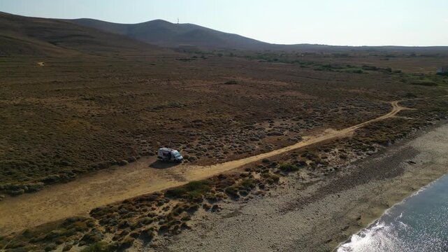 Aerial drone view of a parked campervan at beach Parthenomitos on Limnos Island, Greece. Remote Mediterranean coastal landscape with turquoise sea, rocky shoreline, and peaceful free camping