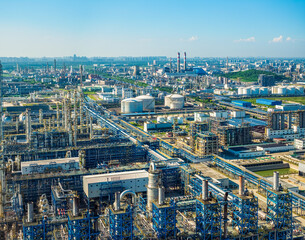 Fototapeta premium High angle view of massive petrochemical plant and chemical industrial zone featuring complex pipelines, storage tanks and processing towers under clear blue sky.
