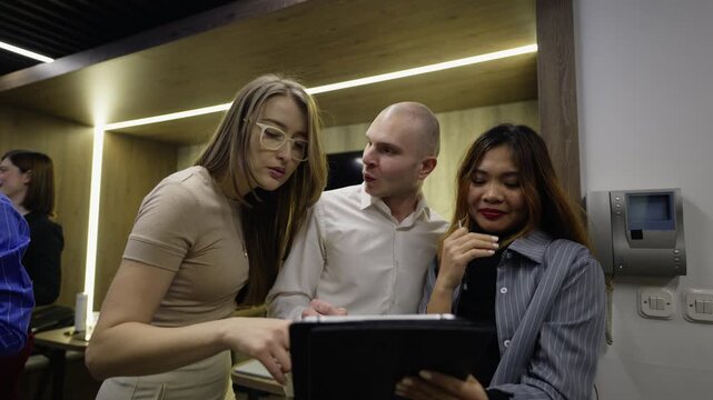 Business colleagues discuss project plans, analyzing data on a digital tablet. The diverse team shares ideas in a modern office.