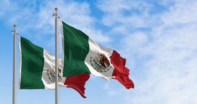 Mexican flags with its coat of arms waving against a blue sky.