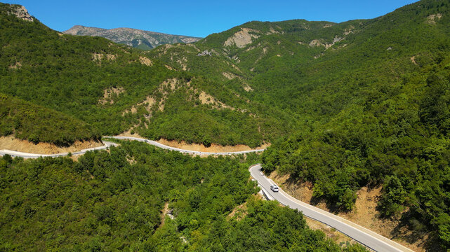 Aerial view of a campervan traveling, driving the iconic SH75 mountain road in Albania, winding through the rugged landscape above the vibrant turquoise waters of the Vjosa River in the summer sun.