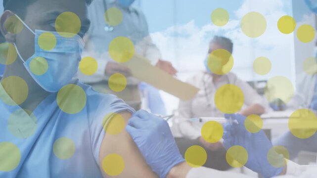 Yellow spots against african american female doctor giving an injection to a man