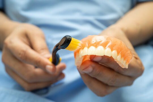 Asian senior woman patient clean teeth denture with toothbrush for chew food.