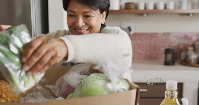 Senior woman unpacking at counter opening box causing animated tags on apples scallions for cooking