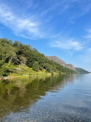 Fototapeta premium Transparent lake water reflecting surrounding forest and mountains. Calm and minimal natural scene with peaceful atmosphere. 