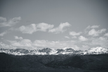 Obraz premium Black and white mountain range with snow covered peaks beneath cloudy skyMonochrome landscape of a snow-covered mountain range under a wide sky filled with soft clouds.