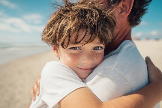 Father and son embracing on a beach, smiling during sunny summer vacation, showing family love and bonding