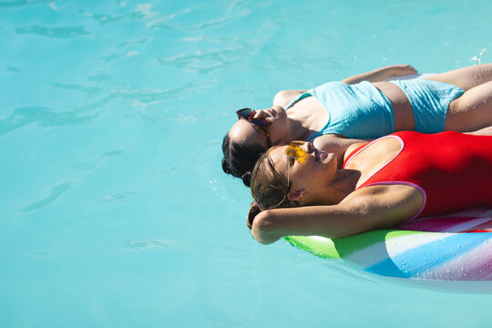 Diverse female friends floating on inflatable ring in outdoor pool, with sunglasses copy space