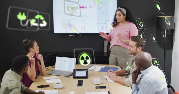 Presenting woman in pink blouse, headband gesturing at CO2 display in conference room with AR icons