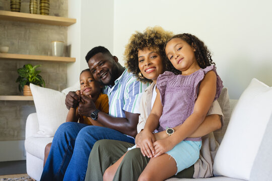Smiling Diverse family sitting on light-colored sofa in modern living room, with wooden shelves