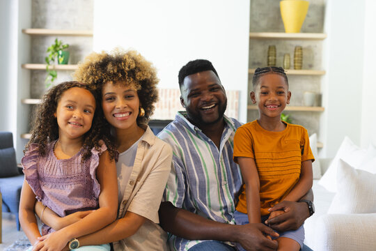 Sitting Diverse family smiling on light sofa in living room, with shelves and plants