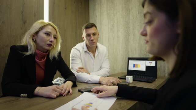 Three business people are discussing financial documents and charts in a modern office. A couple and a female advisor examine paperwork with a positive outcome.