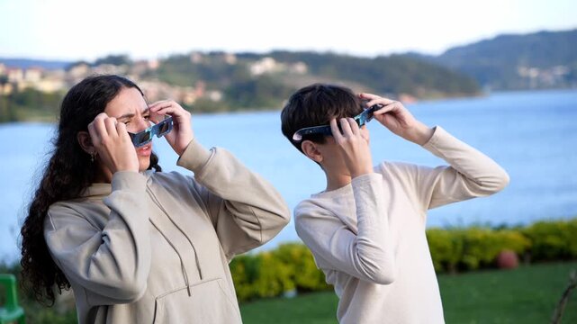Horizontal video of two teenagers observing a solar eclipse with protective glasses outdoors