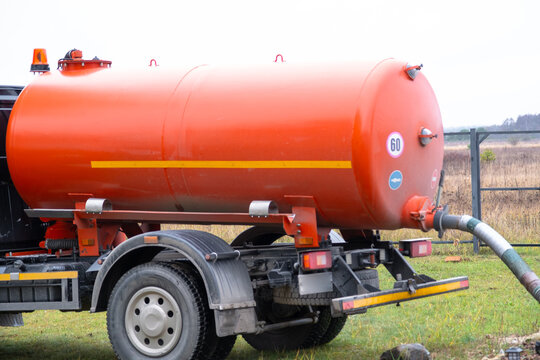 Bright orange vacuum tanker removes sewage from home septic system, septic tank servicing, waste export, sanitation and disposal company.