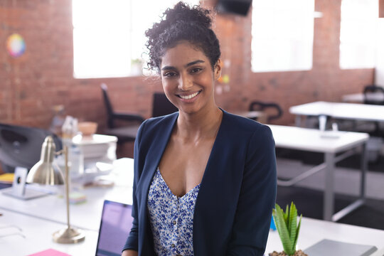 Smiling adult African American woman in blazer working at desk in office using laptop and succulent