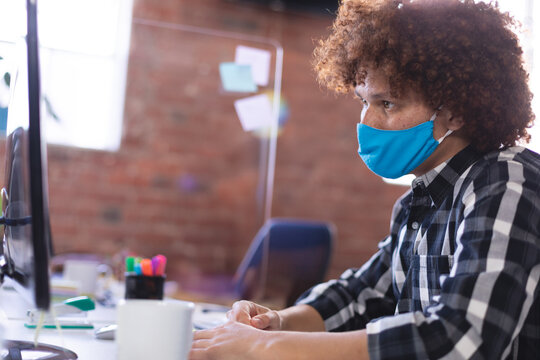 African American man typing on computer at office desk with coffee mug, acrylic divider, copy space