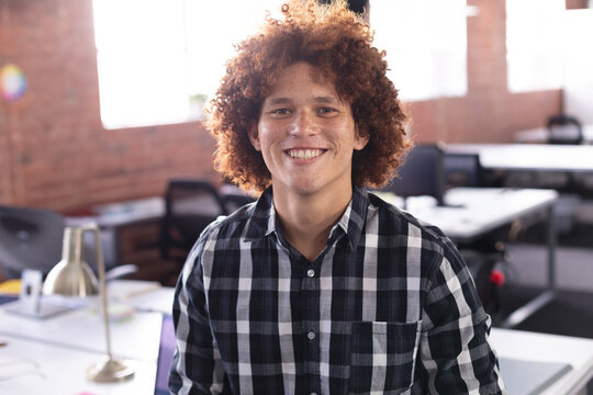 Adult man wearing checkered shirt standing at desk in open-plan office with brass lamp, brick wall