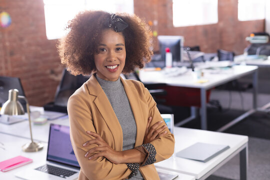 African American woman standing confidently at modern open-plan office desk with laptop, desk lamp