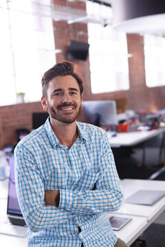 Smiling mid adult man working at workstation in open-plan office using laptop and tablet