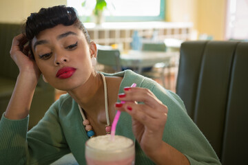 Woman resting head in diner touching straw and starting animated tags around milkshake for food ads © wavebreak3