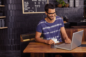 Adult male working at wooden cafe table on laptop under chalkboard menu while holding coffee cup © wavebreak3