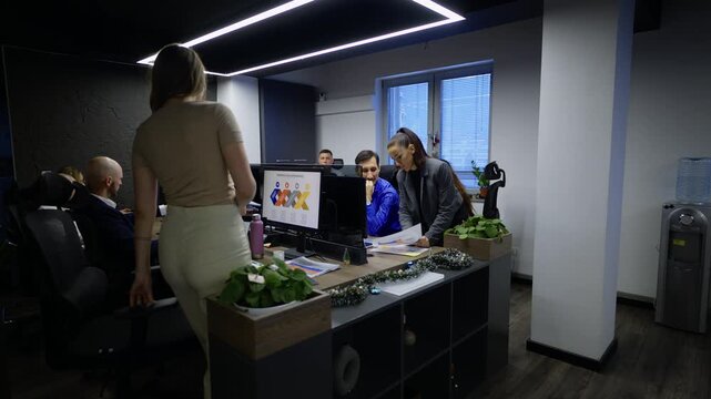 A diverse team of professionals works diligently in a contemporary office environment. They are focused on their tasks, collaborating and discussing projects at their workstations.