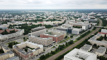 Obraz premium Aerial view of a cityscape with buildings, roads, trees, and a cloudy sky above urban landscape