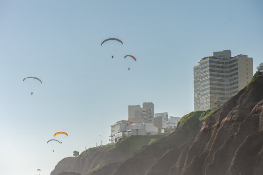 Paragliders Flying Along Lima City Coastal Cliff Beside Urban Buildings Over Clear Blue Sky. Peru