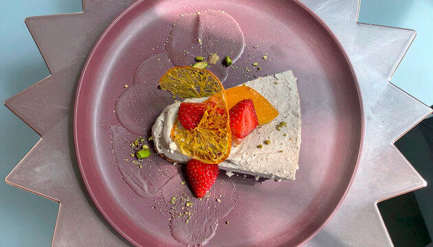 Elegant fruit dessert with cream, strawberry, orange and physalis garnished with pistachio on purple plate