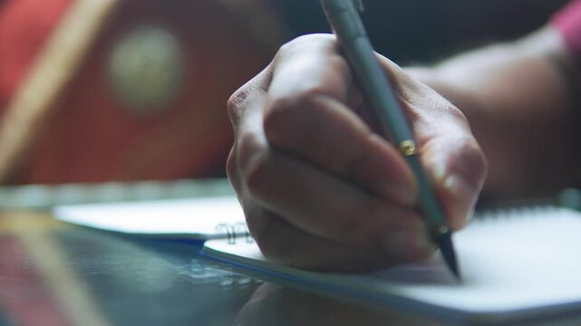 Detailed shot of a person writing or taking notes in a notebook using a classic fountain pen. Soft bokeh background with focused hand movement.
