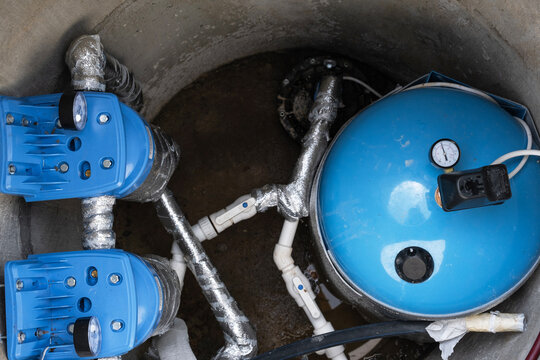 System setup inside artesian well: blue hydrotank, inline water filters, pump motor, reliable water source for home, pump equipment installation and connection.