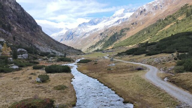 Aerial drone footage of alpine valley with mountain stream winding path and rugged peaks in Zillertal Austrian Alps