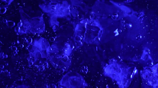 Top view of ice cubes falling into water with splashes and a splash, illuminated by blue light. Concepts for beauty advertising, menu designs for bars and restaurants, cryotherapy.