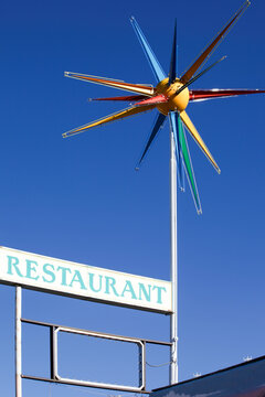 Retro roadside restaurant sign with colorful starburst against blue sky