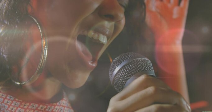 Woman singer holding mic and starting note, belting then easing music, lens flares overlaying face