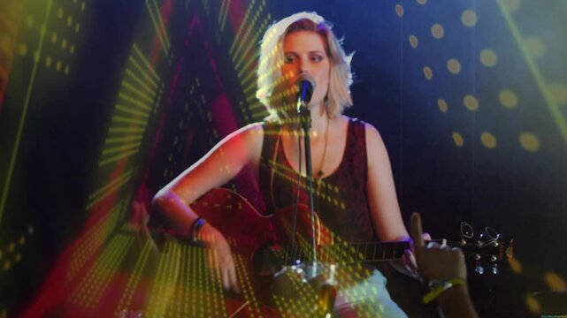 Woman singer playing guitar, singing on 1st chord lights sweeping across her, engaging music fans