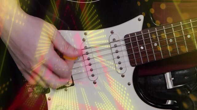 Male guitarist plucking with orange pick, improving picking for music while lights overlay guitar