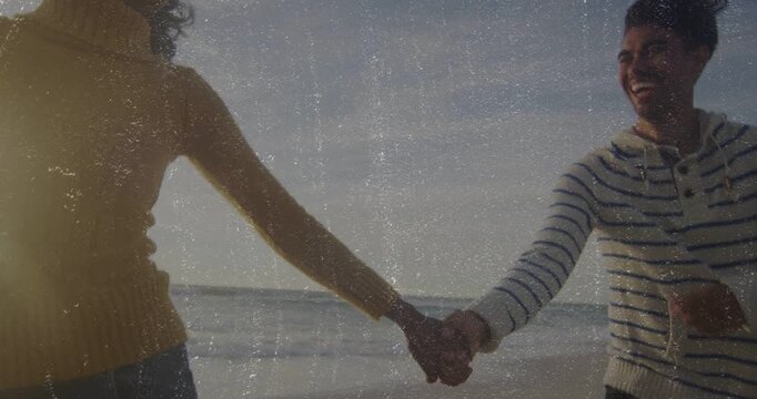 Couple holding hands walking along shoreline, camera pulling back revealing faces for travel ad