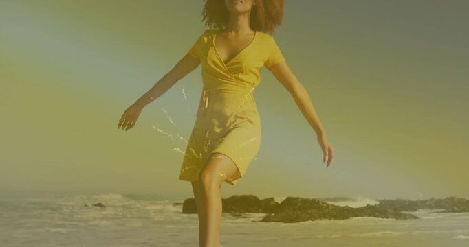 Woman tapping sea and walking sand in yellow dress, camera rising, steps syncing spark for travel