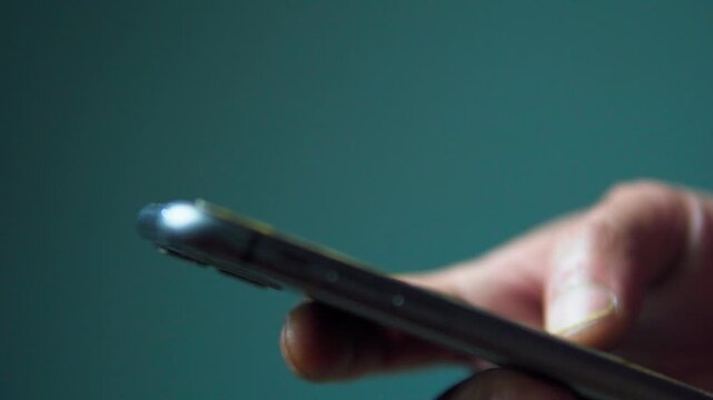 Extreme close up of a thumb scrolling on a mobile phone screen. Detailed view of hand interaction with a smartphone on a clean solid background.
