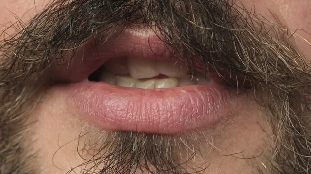 Close up shot of a young caucasian bearded and mustached man mouth speaking silently with no audio. Silent talking lip movement concept.